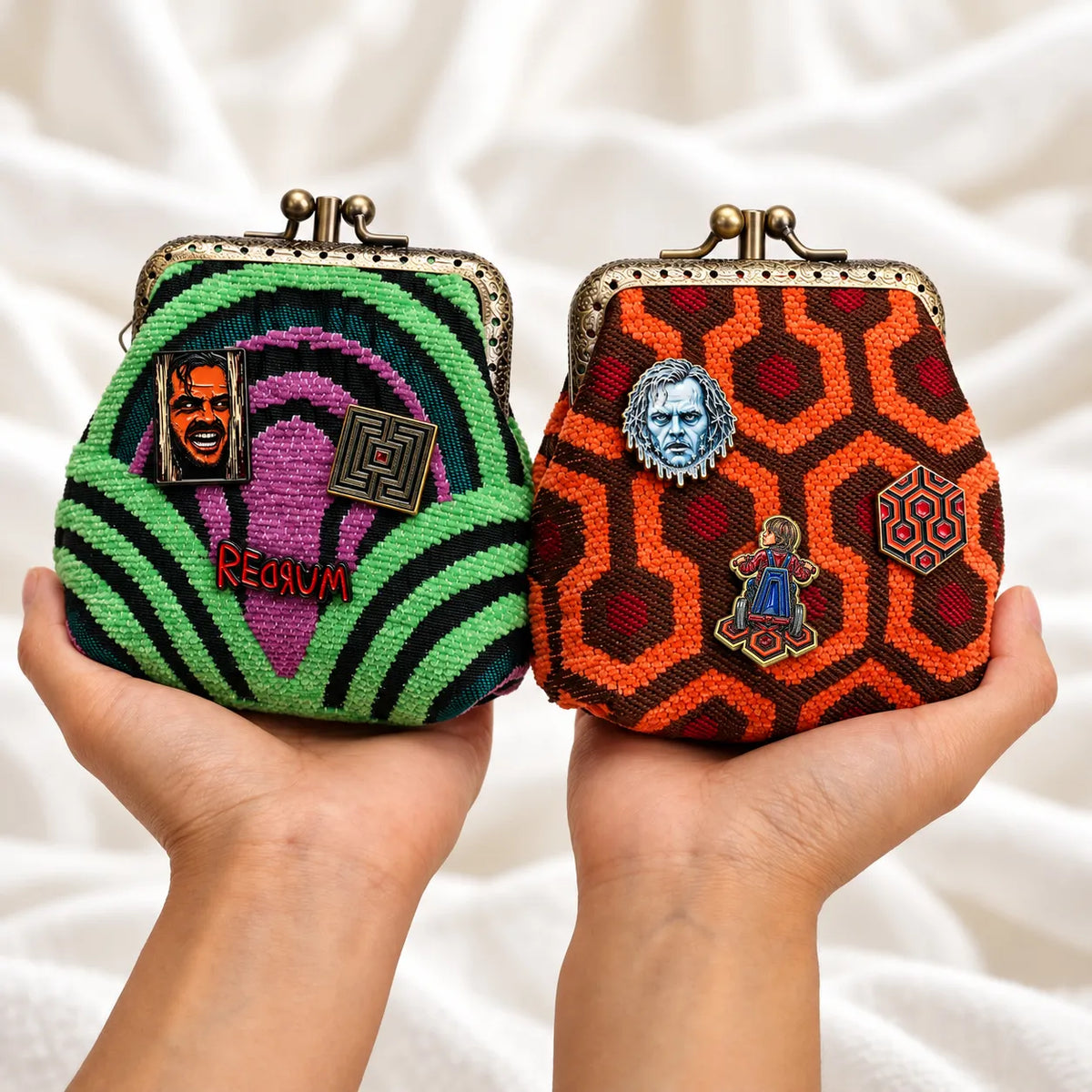 Hands holding green and purple Room 237 and orange Overlook carpet coin purses, each decorated with three The Shining enamel pins.