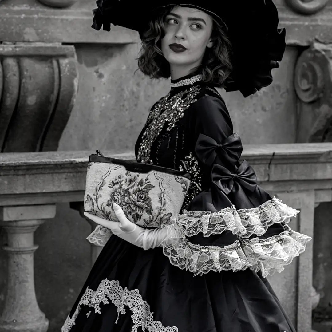 A black-and-white fashion portrait of a woman in vintage clothing holding a floral makeup bag.