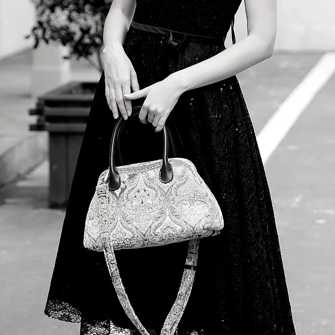 Victorian-inspired chenille carpet handbag with leather handles and detachable shoulder strap, carried by a woman in a black lace dress.
