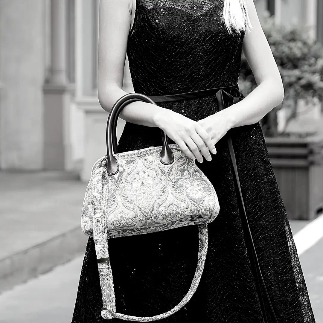 Victorian-inspired chenille carpet handbag with leather handles and detachable shoulder strap, carried by a woman in a black lace dress.