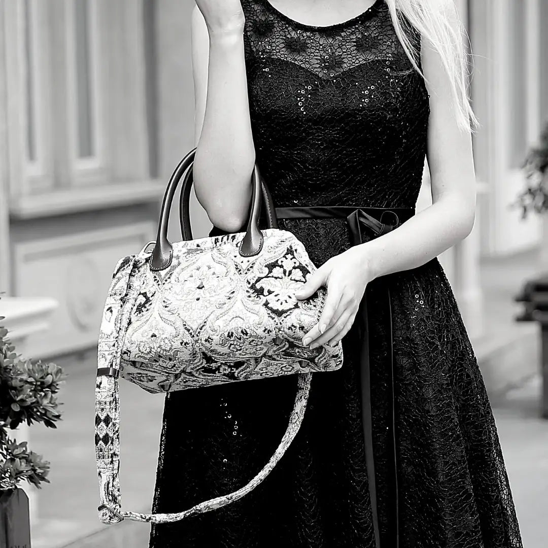 Victorian-inspired chenille carpet handbag with leather handles and detachable shoulder strap, carried by a woman in a black lace dress.