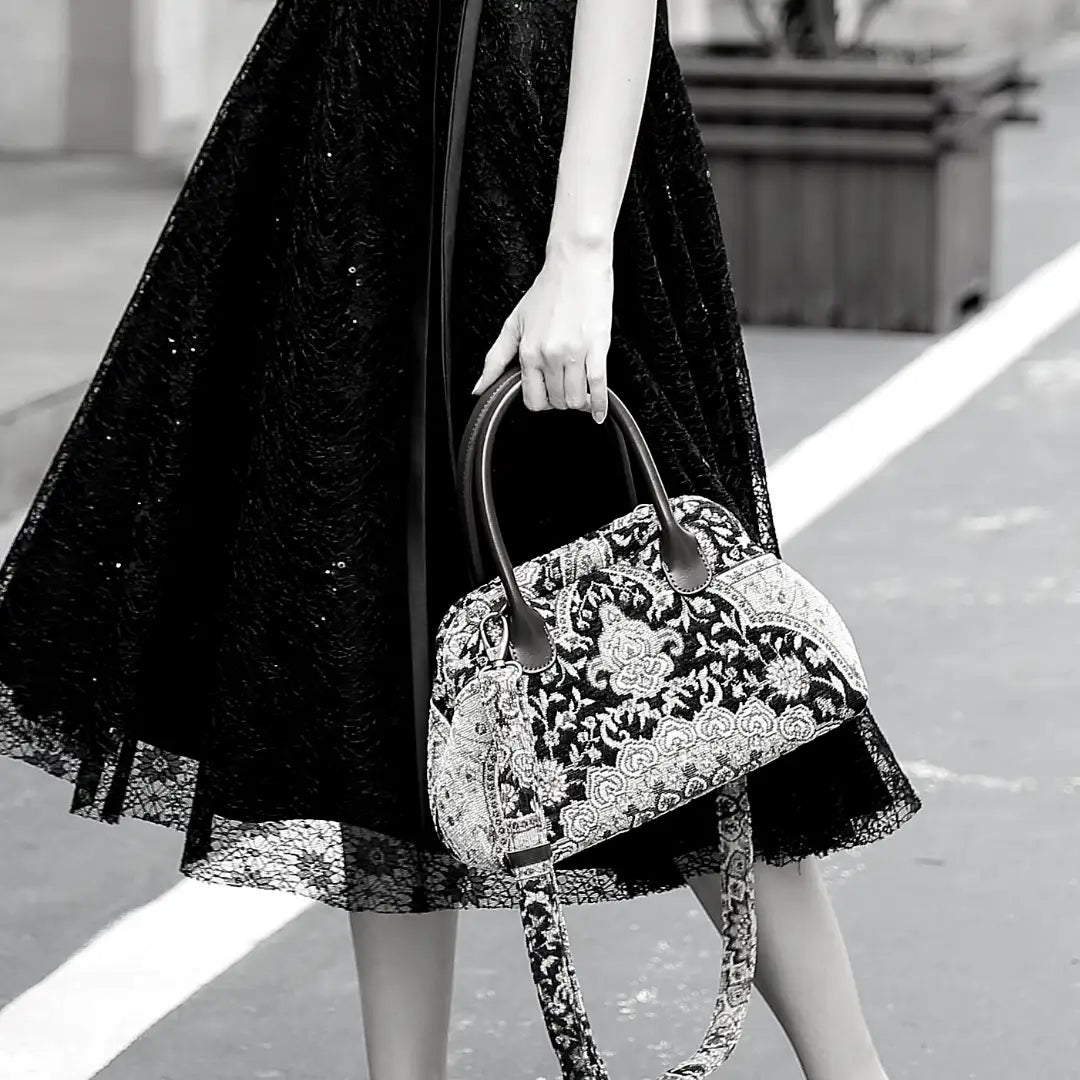 Victorian-inspired chenille carpet handbag with leather handles, carried by a woman in a black lace dress.
