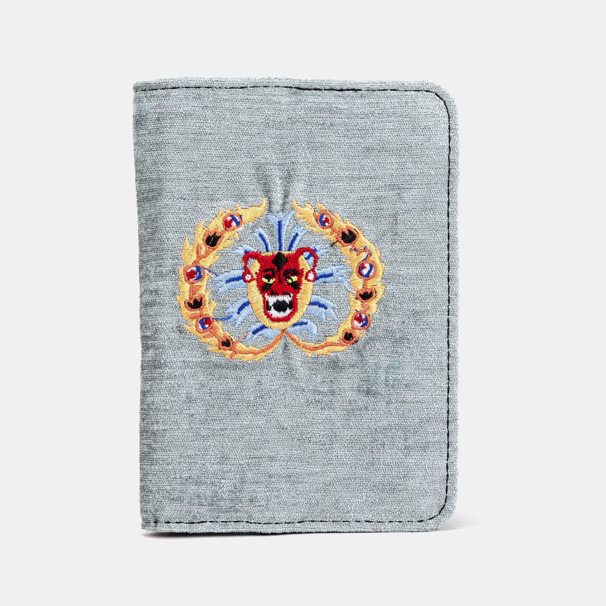 A passport cover with a gray carpet fabric exterior featuring a floral pattern and a red and blue embroidered design on the front, with a lambskin leather lining visible on the inside.