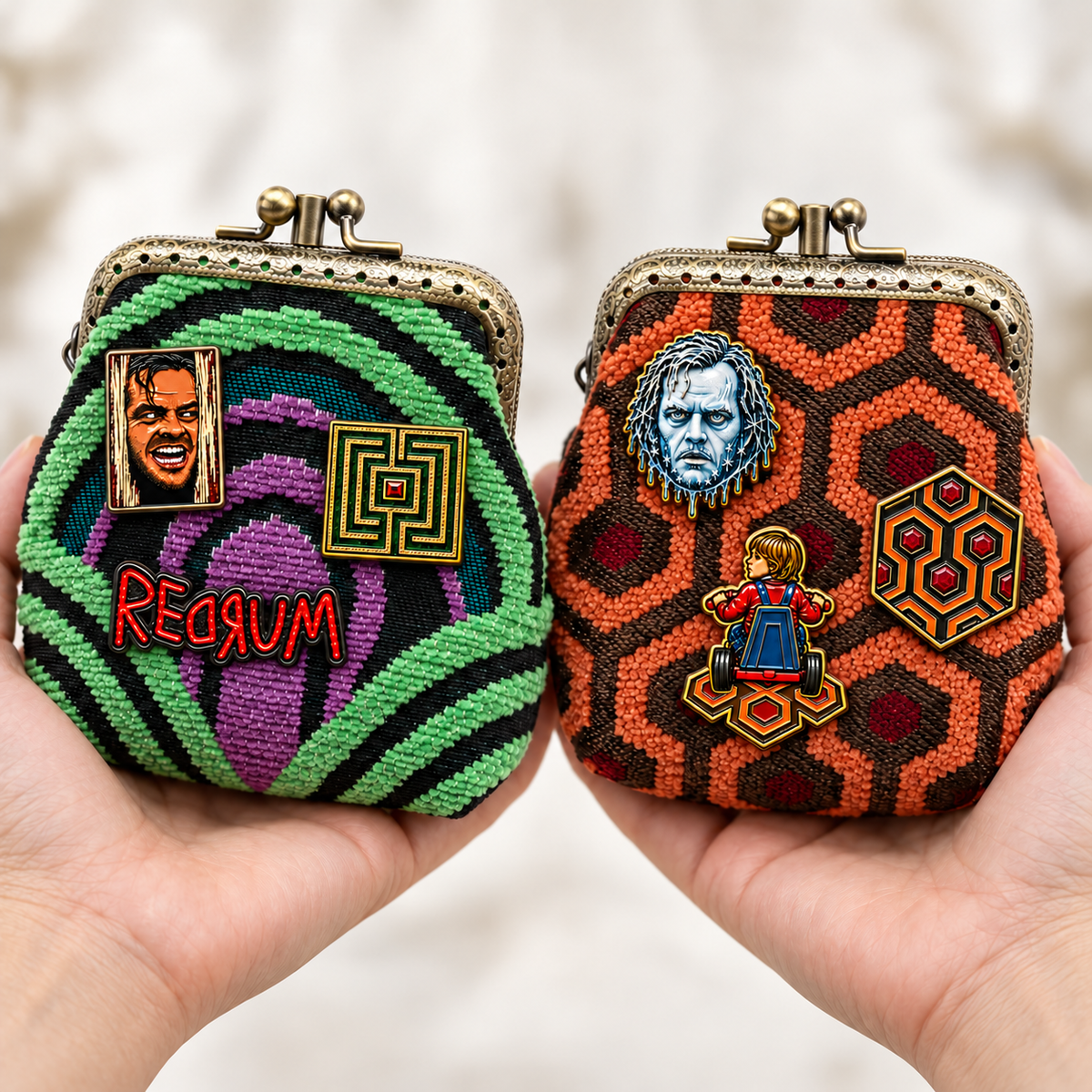 Two kiss-lock coin purses from MCW CARPETBAGS held in hands against a soft blurred light background. The left purse has room 237 carpet pattern and the right has overlook hotel in "the shining" movie, with Enamel pins on them.