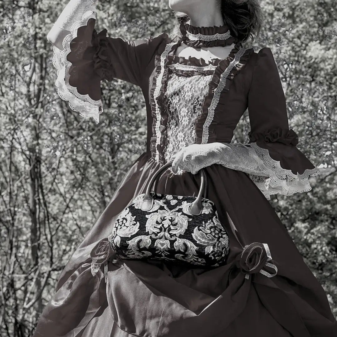 Victorian-inspired chenille carpet handbag with floral damask pattern, carry by a woman in a lace-trimmed vintage dress.