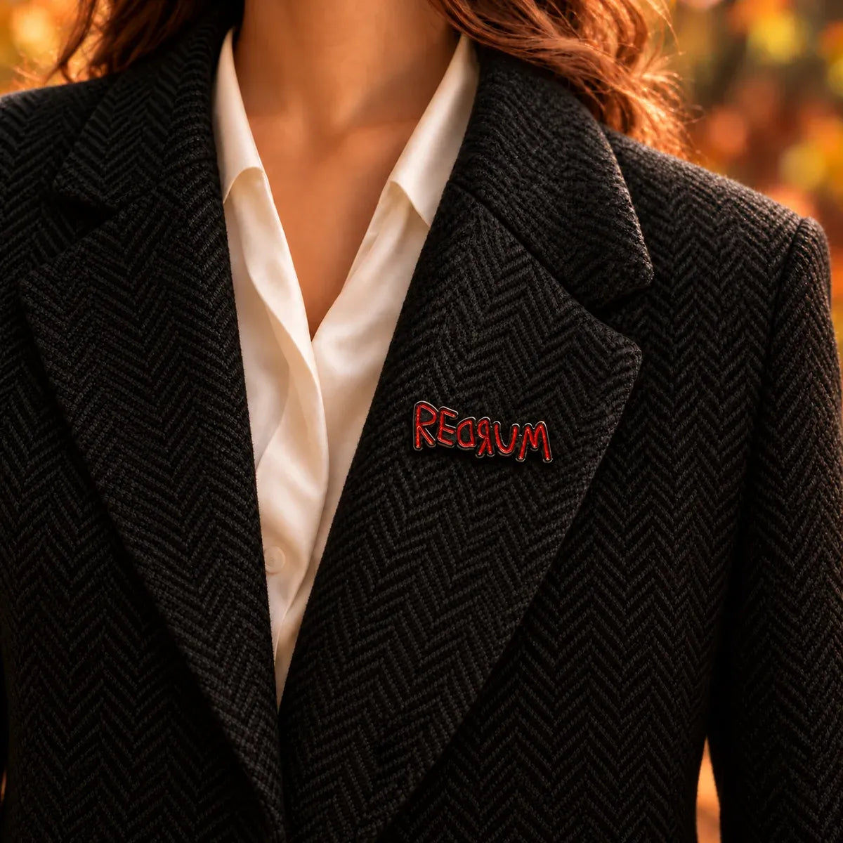 A close-up of a person wearing a black herringbone blazer over a white collared shirt, with a REDRUM Brooch based on movie "The Shining" and it's from MCW handmade company.