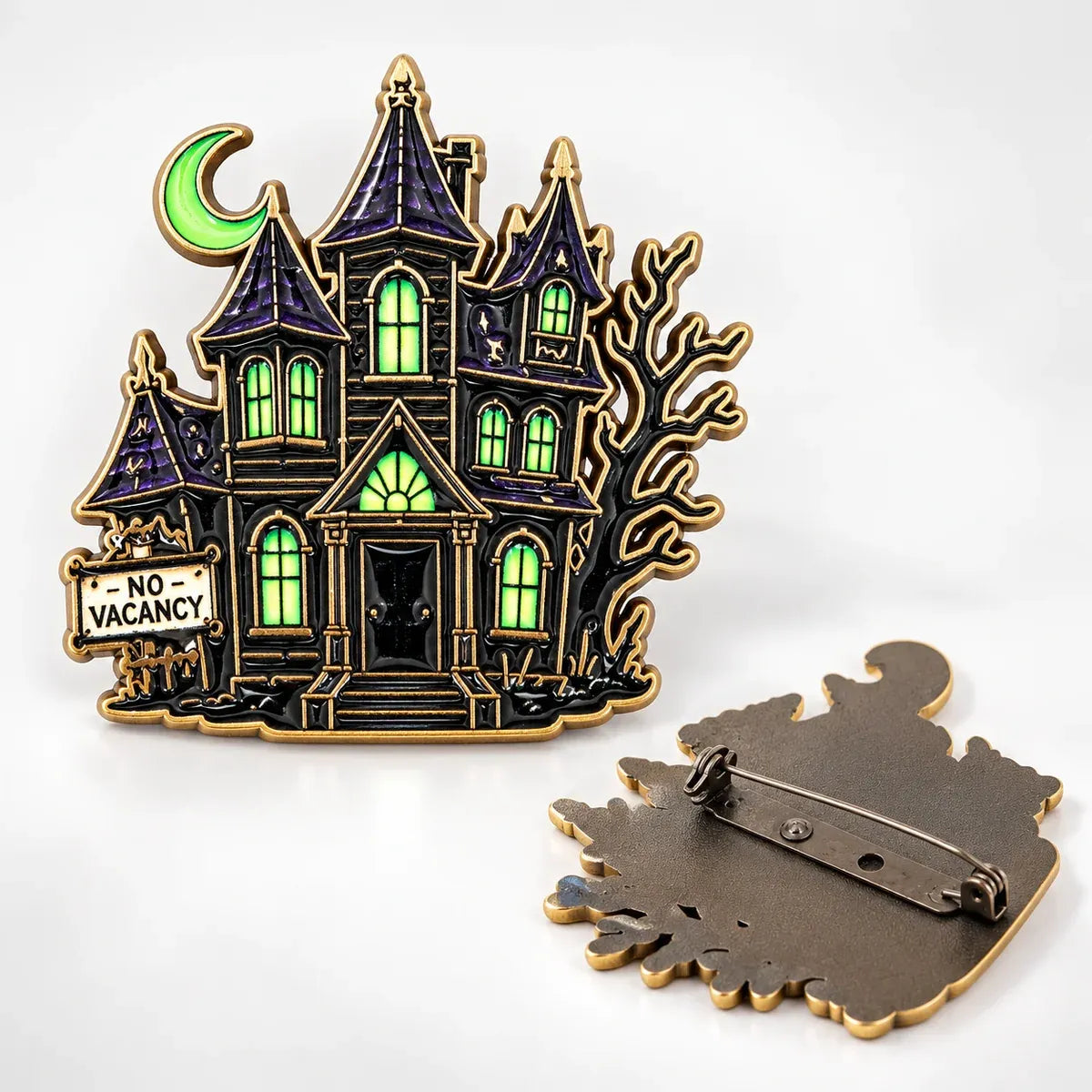 A haunted house enamel brooch from movie Beetlejuice, with a gold-tone outline, featuring dark purple roofs, glowing green windows, a green crescent moon, a bare tree, and a 'No Vacancy' sign. The back of the pin is shown separately on a white background.