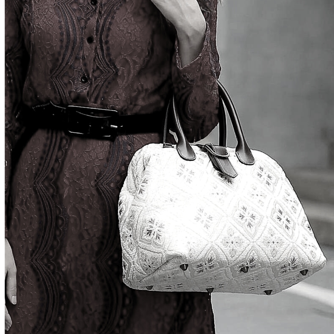 Woman wearing a red sequined dress carrying a vintage-inspired carpet handbag with leather handles.