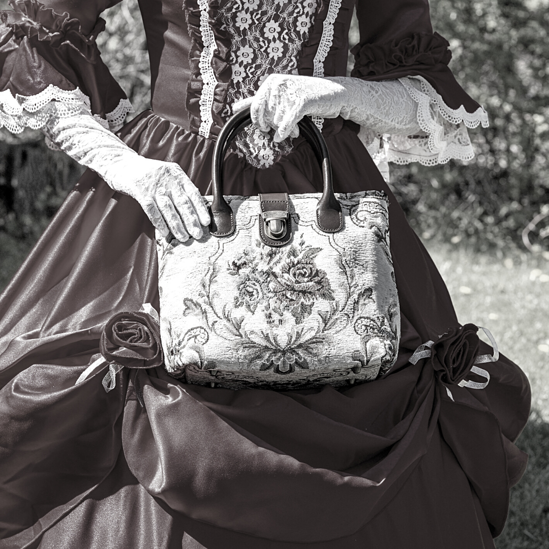 Victorian-style woman holding a floral tapestry handbag while wearing a lace-trimmed historical dress.