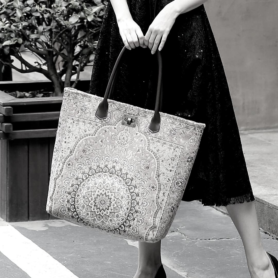 Victorian-inspired carpet tote bag with leather handles and intricate medallion pattern, carried by a woman in a black lace dress.
