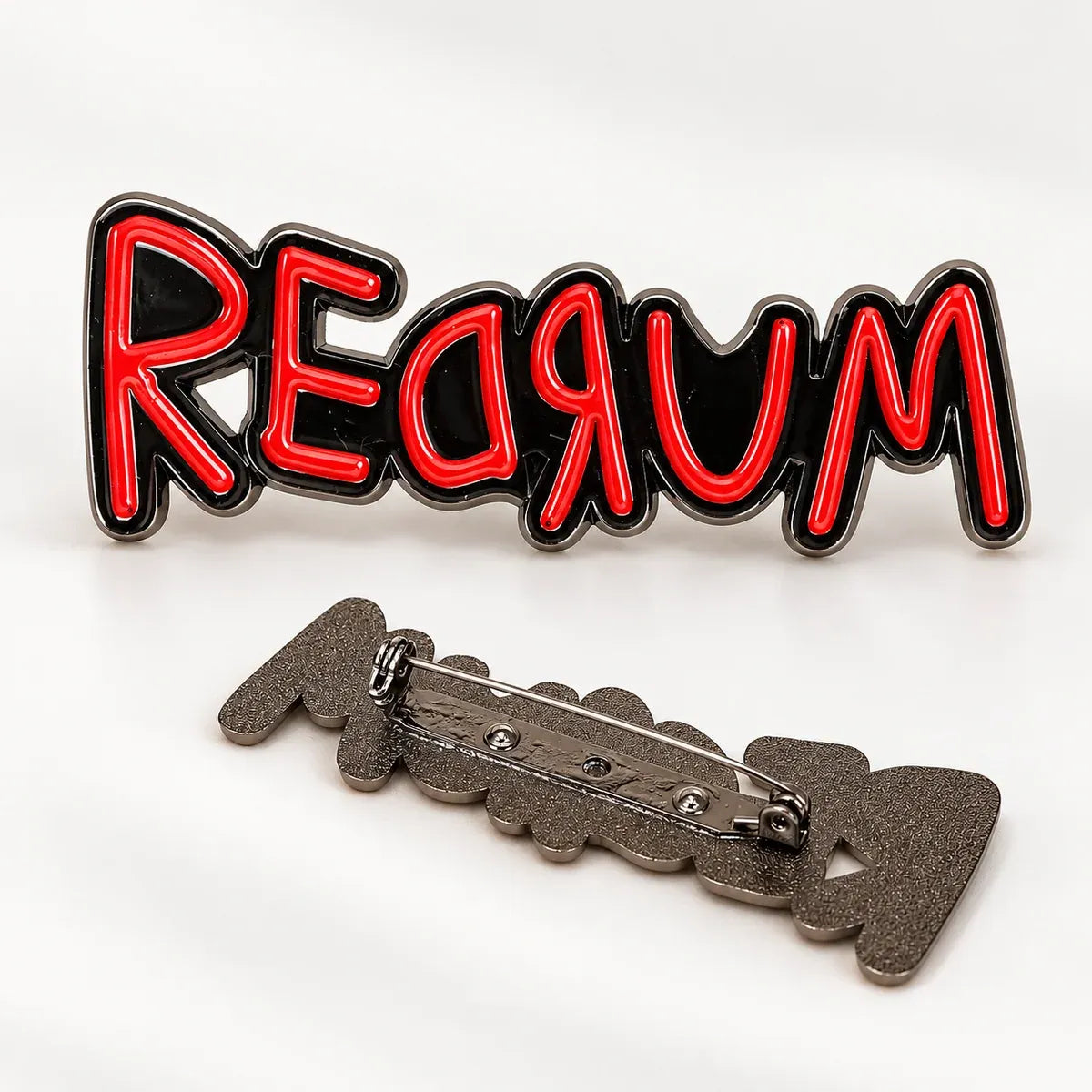 A novelty pinback badge spelling 'MURDER' in red neon-style lettering with a black outline, shown alongside the back of the badge featuring a textured dark gray metal clasp.