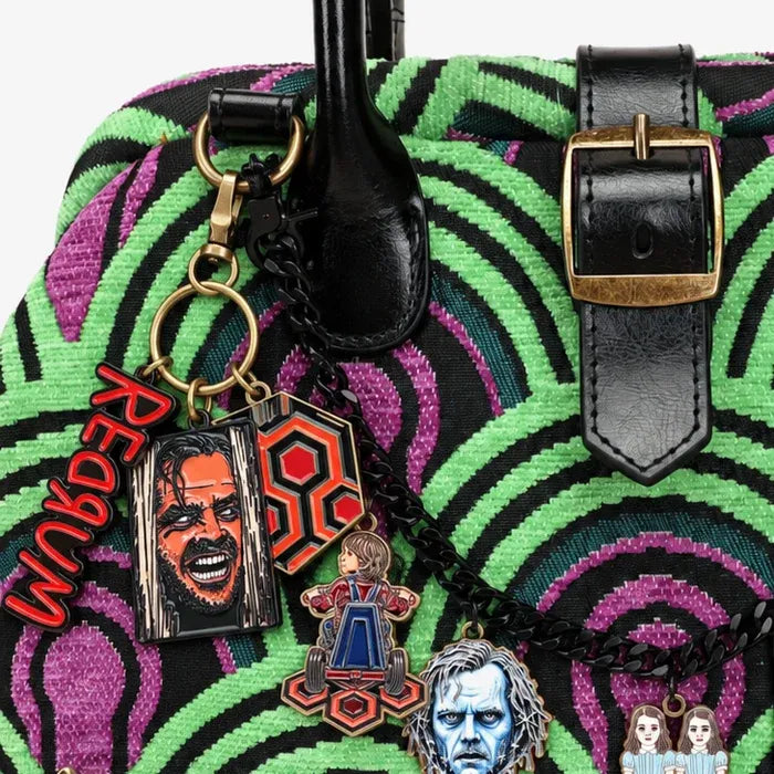 A close-up of a handbag featuring a bold green, black, and purple psychedelic spiral pattern. Including a prominent buckle and a hanging keychain with multiple character charms.