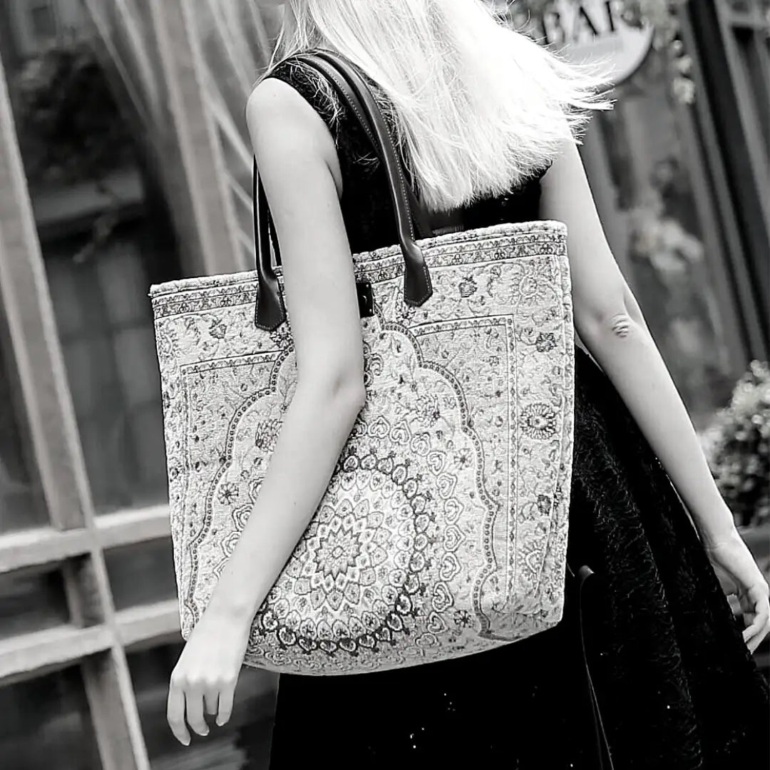 Victorian-inspired carpet tote bag with leather handles and intricate medallion pattern, carried by a woman in a black lace dress.
