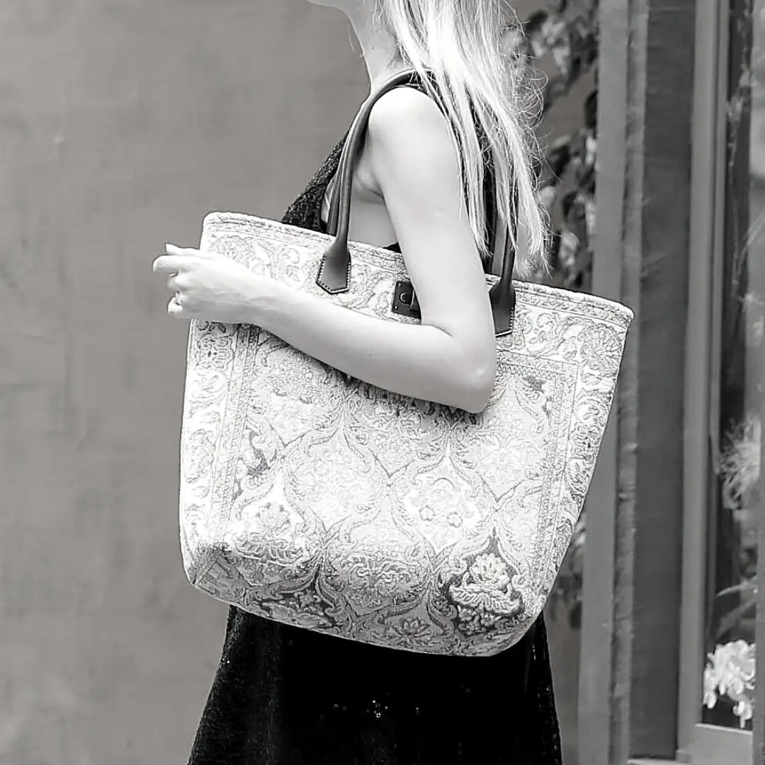 Large floral tapestry tote bag with brown leather handles, carried by a model in a black dress. Features an elegant Victorian-inspired pattern and spacious interior for everyday use.