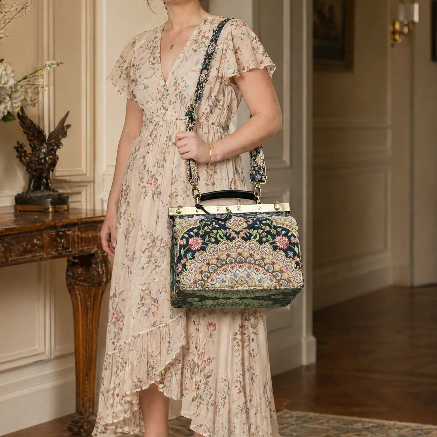 Woman in a floral dress holding an oriental navy vivienne purse gladstone bag in an elegant interior setting