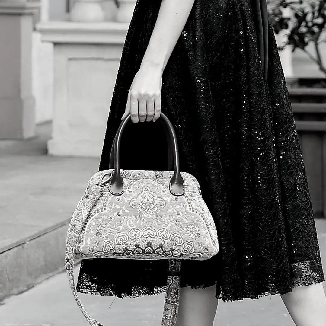 Victorian-inspired chenille carpet handbag with leather handles and detachable shoulder strap, carried by a woman in a black lace dress.