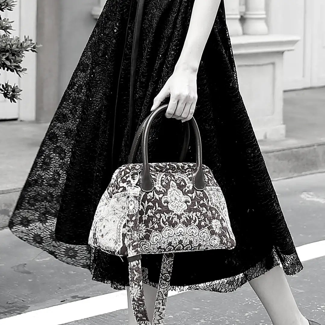 Victorian-inspired chenille carpet handbag with genuine leather handles and a detachable shoulder strap, carried by a woman in a black lace dress.