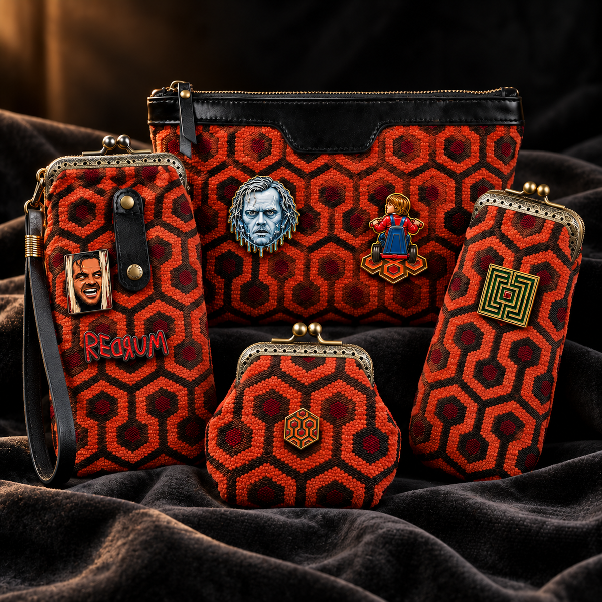A coordinated set of red and black patterned accessories arranged on dark velvet fabric, the products are carpet bags from MCW HANDMADE, including a large zip pouch, wristlet, coin purse, and small pouch, each decorated with character portrait pins and a hexagon motif. they are decorated with "The Shining" Enamel pins.