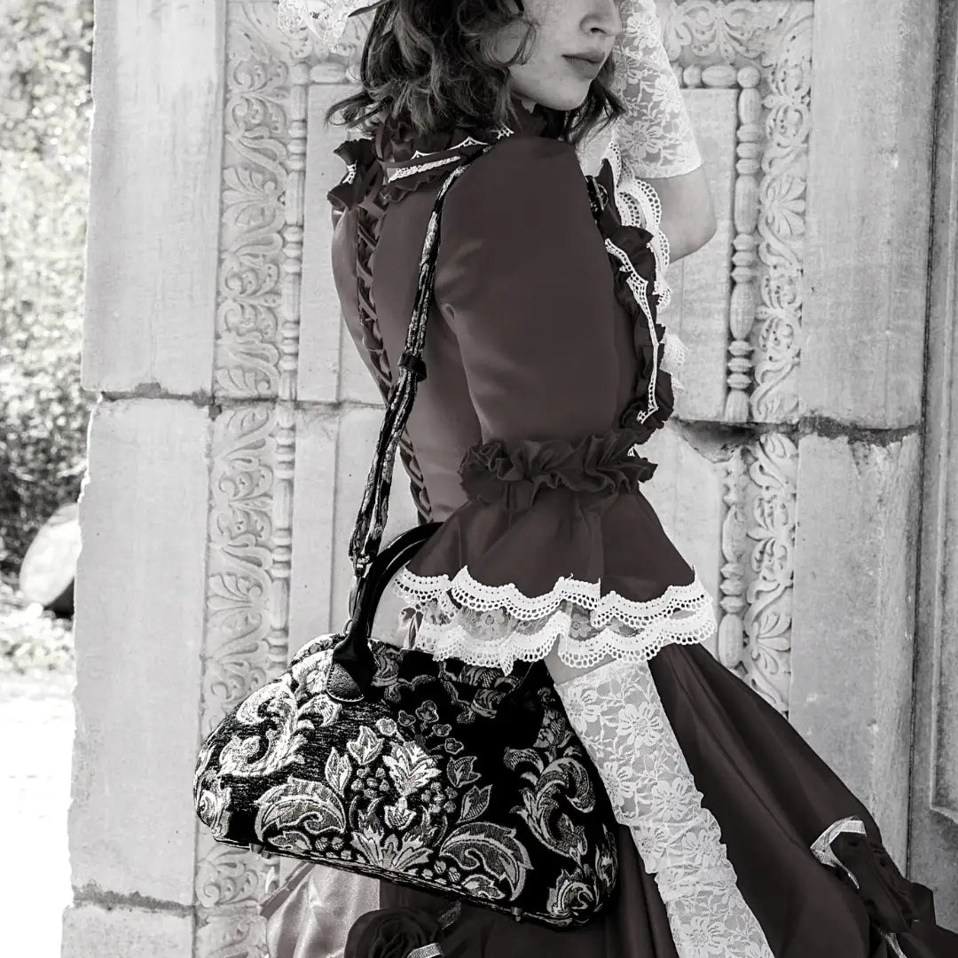 Victorian-inspired chenille carpet handbag with floral damask pattern, worn over the shoulder by a woman in a lace-trimmed vintage dress.