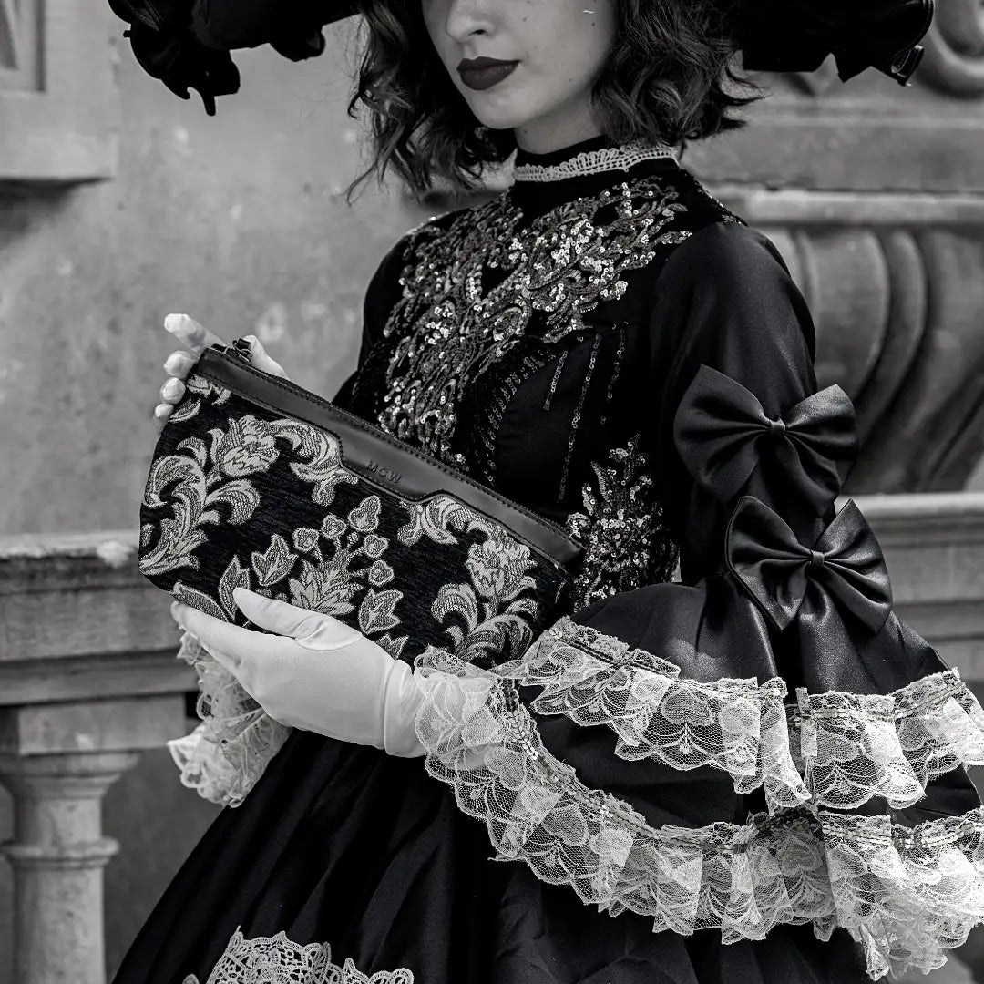 A black-and-white fashion portrait of a woman in vintage clothing holding a floral makeup bag.