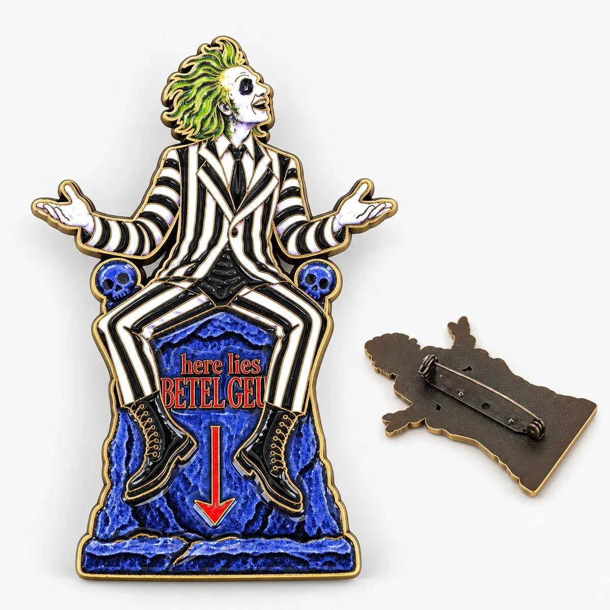An enamel brooch of the character Beetlejuice from MCW HANDMADE, seated on a blue crackled base with the text 'here lies BETEL GEI' and a red arrow, shown alongside the metal pin backing on a white background.
