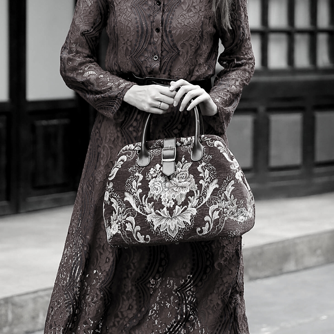 Woman wearing a red sequined dress carrying a vintage-inspired carpet handbag with leather handles in an elegant city setting.