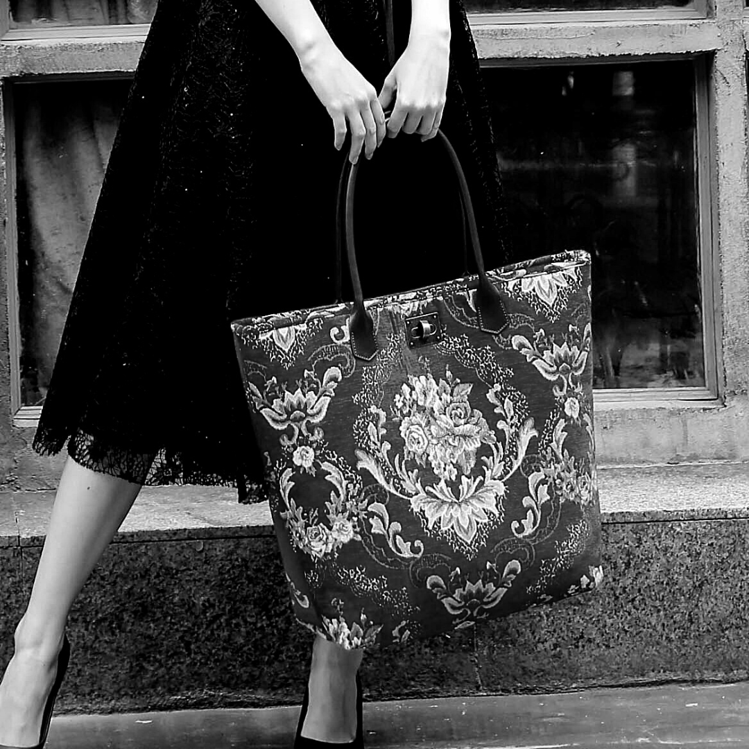 Large floral tapestry tote bag, featuring an ornate Victorian-inspired rose pattern. Shown carried by a model in a black dress, highlighting its spacious design and elegant vintage style.