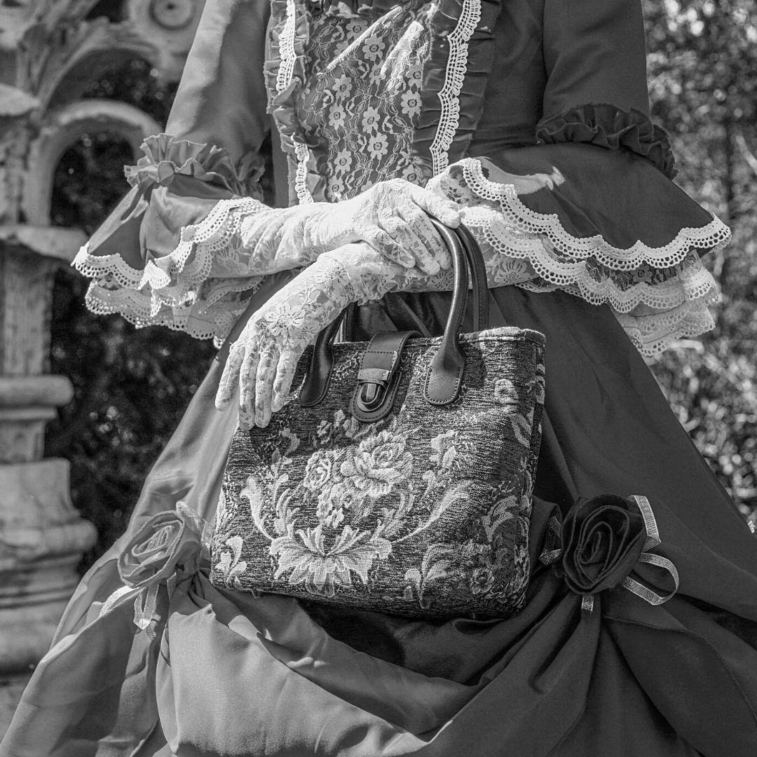 Victorian-style woman holding a floral tapestry handbag while wearing a lace-trimmed historical dress.