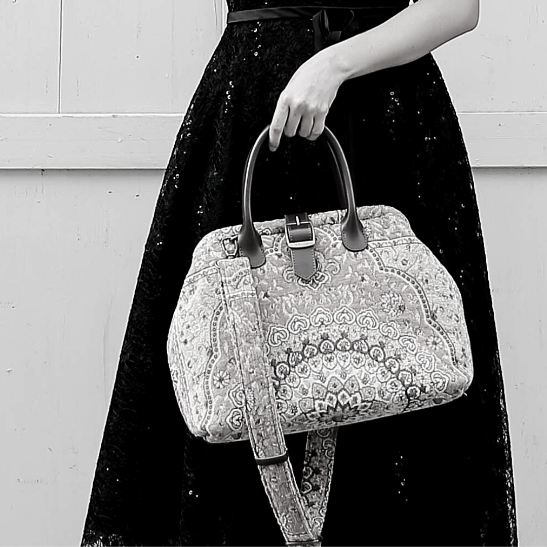 Woman wearing a black sequined dress carrying a vintage-inspired carpet handbag with leather handles and shoulder strap.